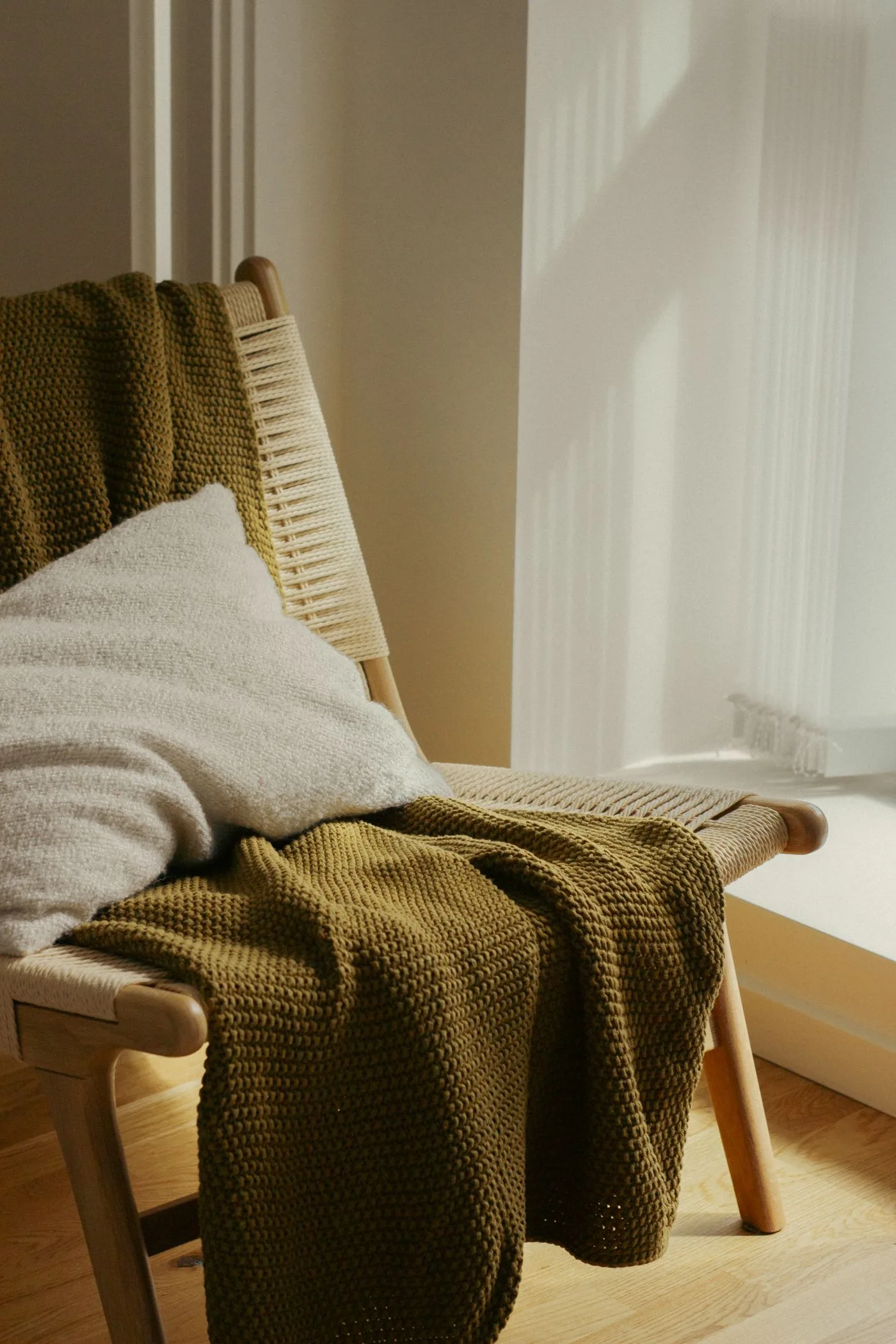 A stylish chair with green blanket and pillow in sunlit room, perfect for cozy interiors.