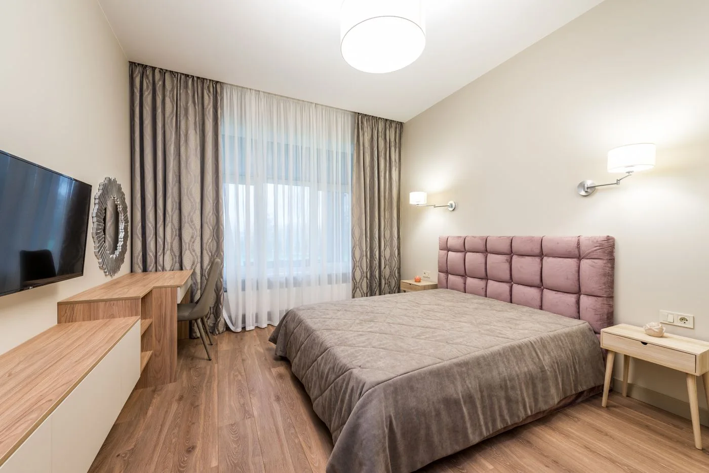 A bedroom with a wall-mounted screen, curtains and a quilted headboard