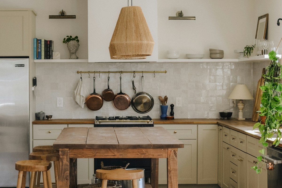 A rustic kitchen with a wooden table, stools and hanging cookware
