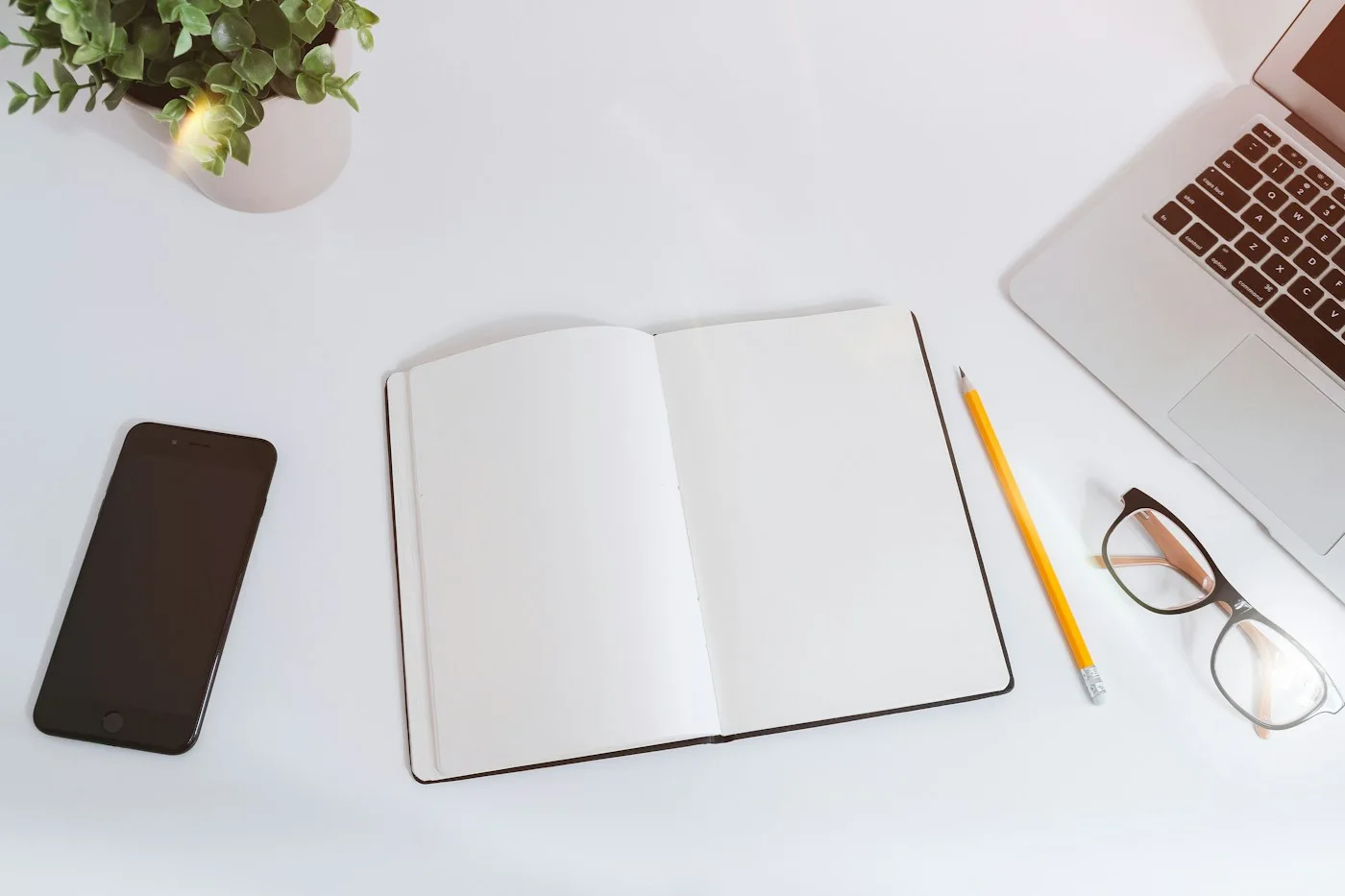 Notebook, pen, glasses, and devices arranged on a white desk