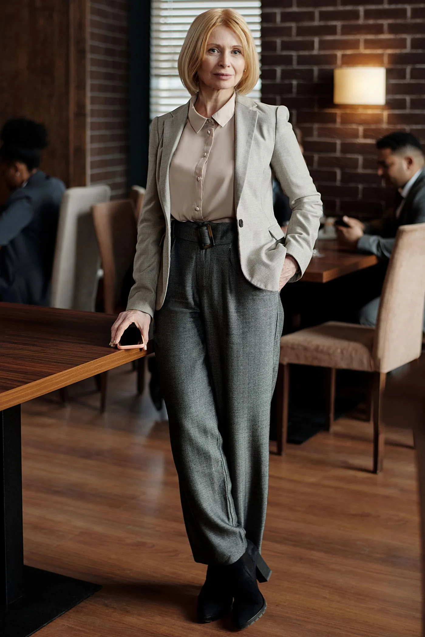 Woman in a beige blazer, light blouse and gray trousers beside a table