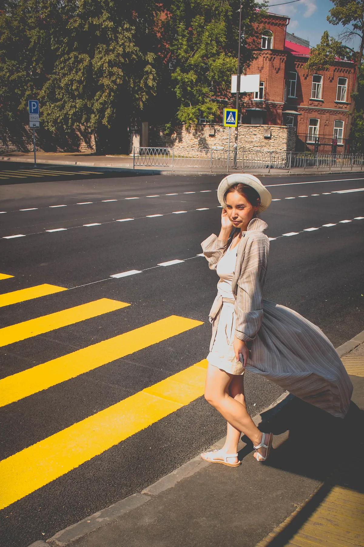 A woman wearing a light dress and hat on a city crossing