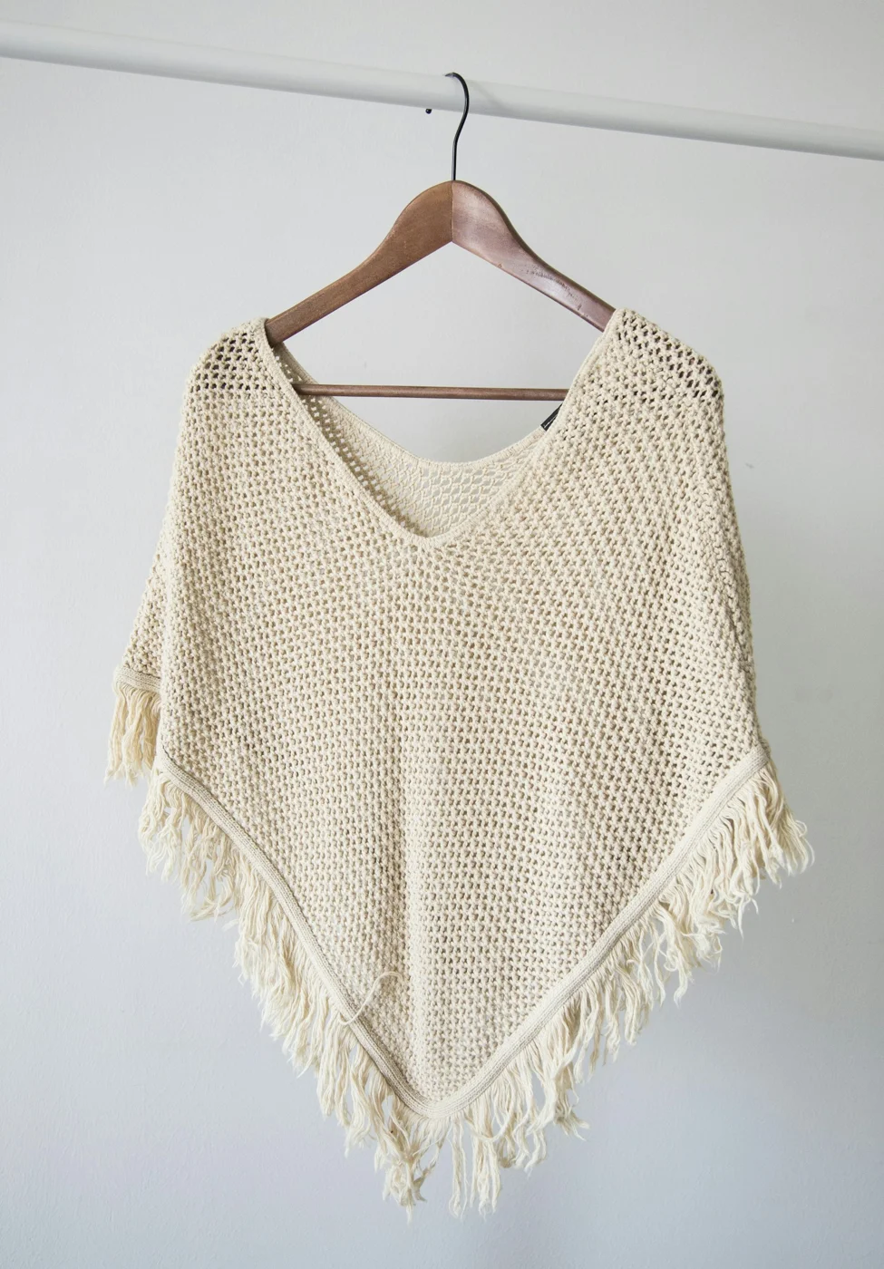 A cream knit garment hanging on a wooden hanger