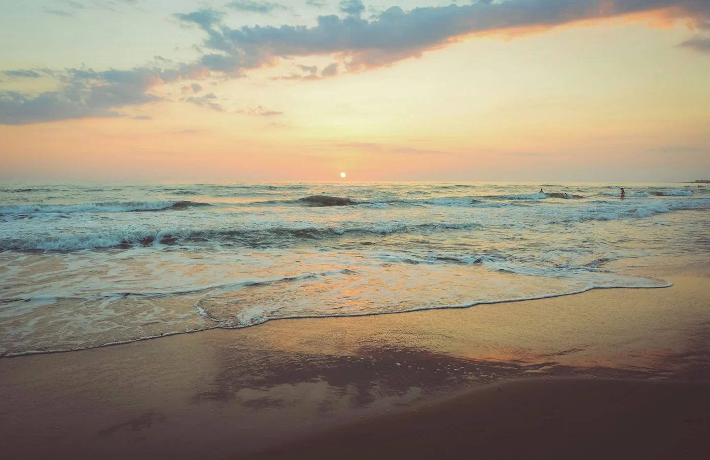 Gentle ocean waves along a sandy beach at sunset