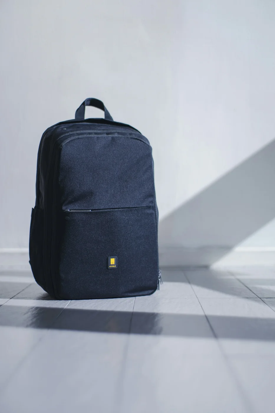 A compact dark backpack standing against a wall